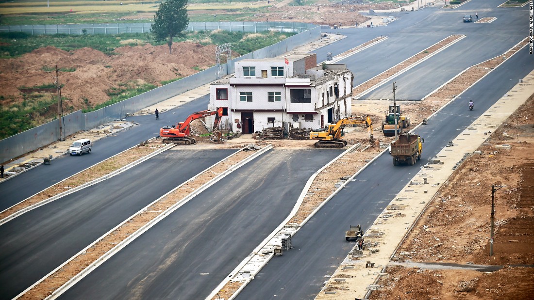 A three-story house stands in the middle of a newly built road in China&#39;s Henan province on May 16, 2015. Construction was put to a halt as the owner refused to move because of a dispute about compensation. Like a nail that refuses to be hammered down, the dwelling is one of many &quot;nail houses&quot; that have sprung up in China as some homeowners resist development of their land or hold out for more money. According to construction workers, the owner is still living inside the house even though the rest of the road is complete.