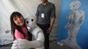 &#39;Pepper,&#39; a robot with emotional capabilities hugs a girl at DARPA Robotics Challenge on June 5, 2015.