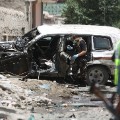 Afghan security personnel inspect a damaged vehicle at the site of a suicide attack that targeted a NATO convoy in Kabul, Afghanistan, Tuesday, July 7, 2015. An Afghan official said the attack by a suicide car bomber in the capital, Kabul, wounded at least two people. (AP Photo/Rahmat Gul)