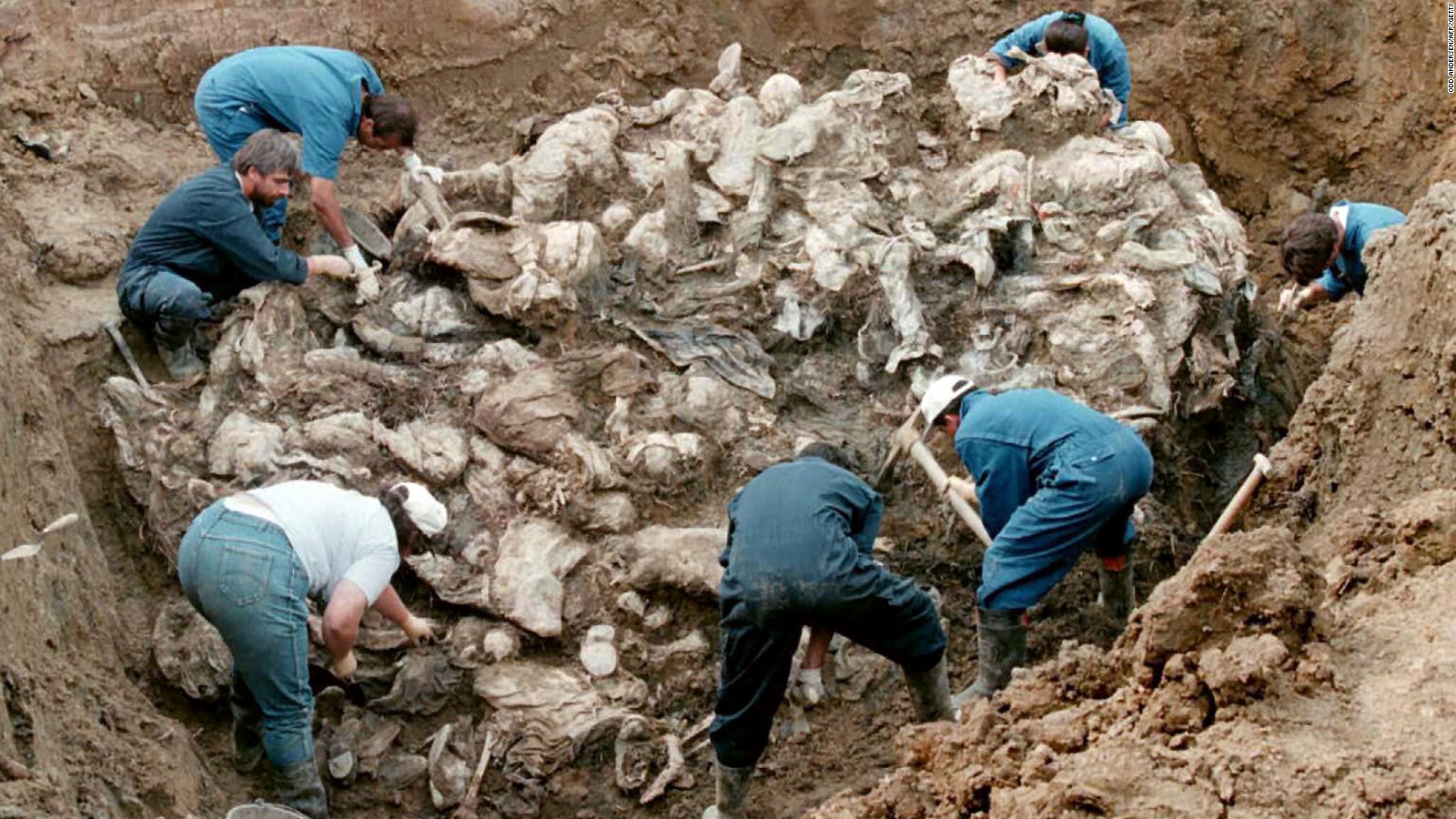 Investigators and forensic experts work on top of a cluster of bodies, many of them with their hands tied in the back and many of them blindfolded