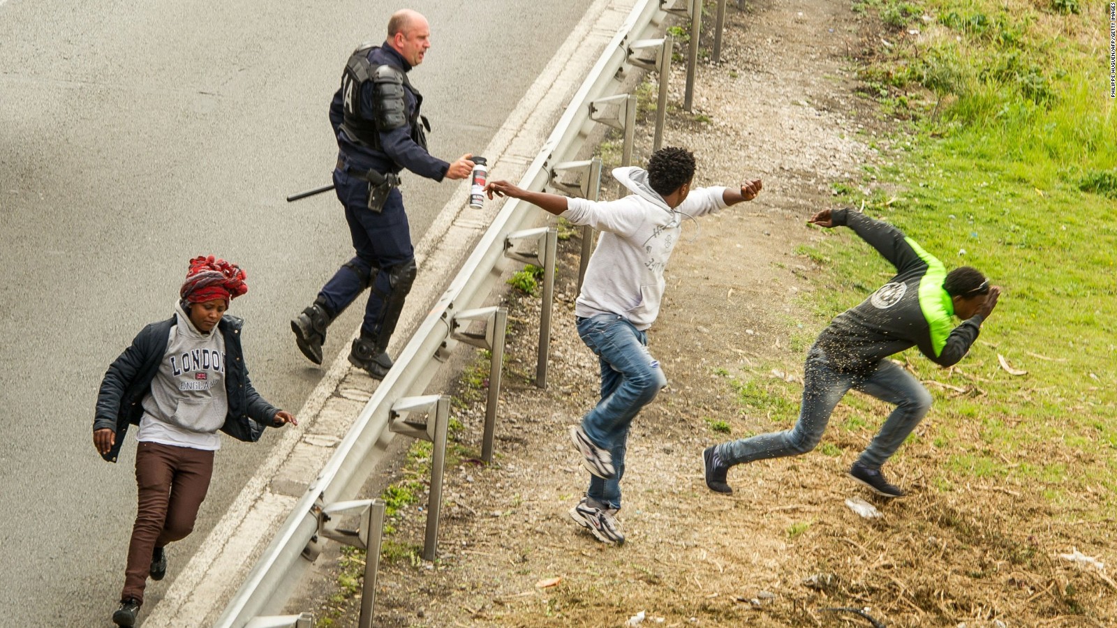 A police officer sprays tear gas at migrants trying to access the Channel Tunnel in Calais, northern France, to get to Britain.