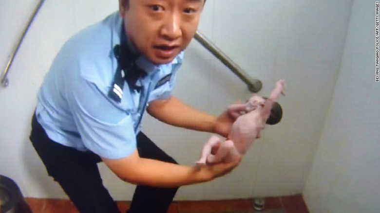 An image supplied by police shows an officer holding the baby in a Beijing toilet block, August 2, 2015.
