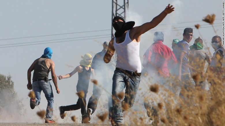 A Palestinian man on Saturday throws a tear gas canister back during clashes with Israeli security forces after the funeral of the father of a Palestinian toddler killed when their home was firebombed by Jewish extremists.