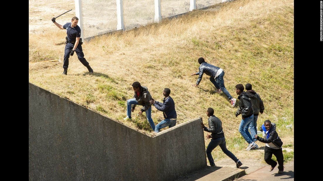 A police officer in the northern French city of Calais tries to prevent migrants from heading for the Channel Tunnel to England on Wednesday, June 17.