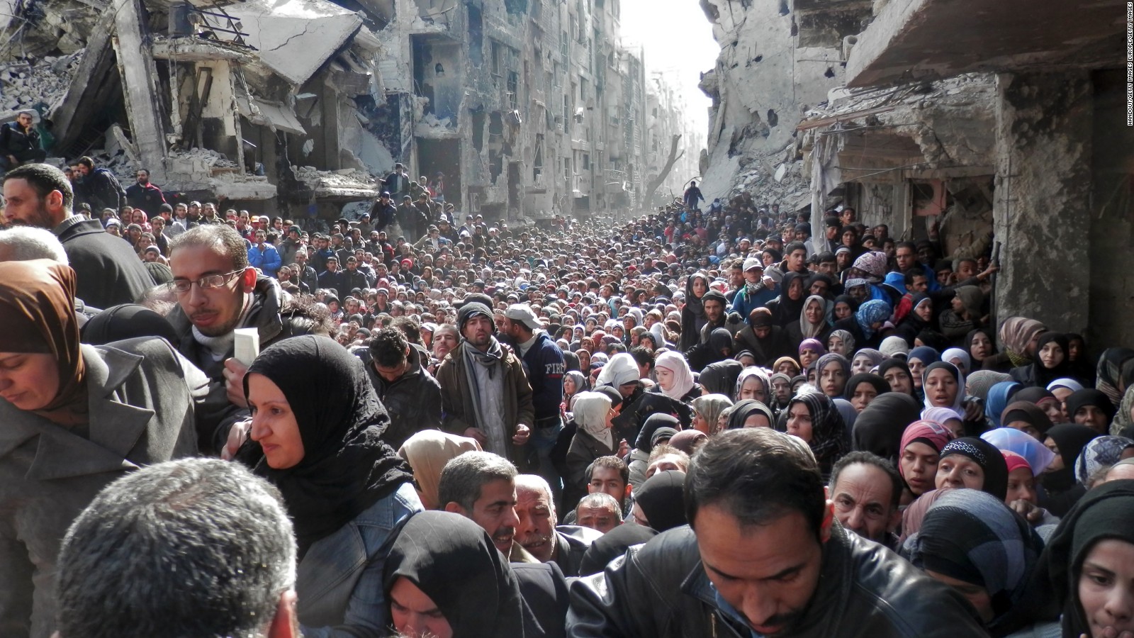 DAMASCUS, SYRIA - JANUARY 31: In this handout provided by the United Nation Relief and Works Agency (UNRWA), Residents wait in line to receive food aid distributed in the Yarmouk refugee camp on January 31, 2014 in Damascus, Syria. The United Nations renewed calls for the Syria regime and rebels to allow food and medical aid into the Palestinian camp of Yarmouk. An estimated 18,000 people are besieged inside the camp as the conflict in Syria continues. (Photo by United Nation Relief and Works Agency via Getty Images)