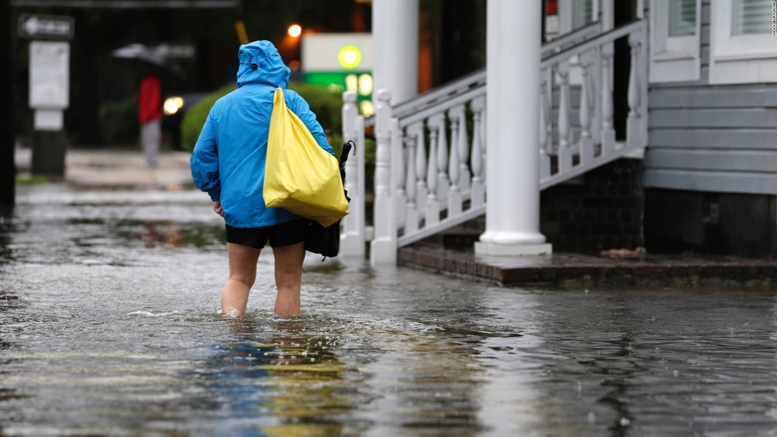 A woman walks down a flooded sidewalk toward an open convenience store in Charleston, South Carolina, on Sunday, October 4.