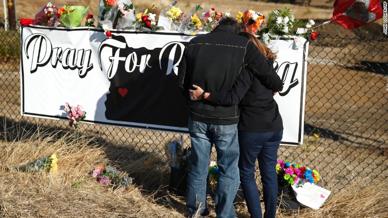 Two people embrace as they place flowers at a makeshift memorial near the road leading to Umpqua Community College