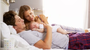 Stock Photo:
Family In Bed Holding Sleeping Newborn Baby Daughter