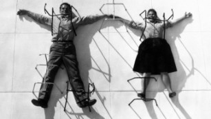 Charles and Ray Eames posing with chair bases.
