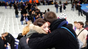 Spectators embrace each other as they stand on the playing field of the Stade de France stadium at the end of a soccer match between France and Germany in Saint Denis, outside Paris, on November 13.