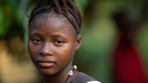[NAME CHANGED] On 14 November 2015, Amina Kamara, 15, stands in the yard of her home,  behind her is her husband Lamine, in Motonko Village, Ribbi Chiefdom, Moyamba District.

