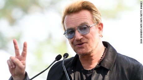 Bono holds up a peace sign during a dedication ceremony for a giant tapestry, from Amnesty International, in honor of John Lennon on Ellis Island July 29, 2015 in New York. AFP PHOTO/DON EMMERT        (Photo credit should read DON EMMERT/AFP/Getty Images)