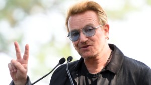 Bono holds up a peace sign during a dedication ceremony for a giant tapestry, from Amnesty International, in honor of John Lennon on Ellis Island July 29, 2015 in New York. AFP PHOTO/DON EMMERT        (Photo credit should read DON EMMERT/AFP/Getty Images)