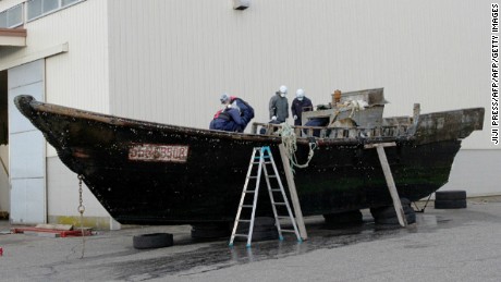 This picture taken on November 24, 2015 shows coast guard officials investigating a wooden boat at the Fukui port in Sakai city in Fukui prefecture, western Japan after the ship was found drifting off the coast of Fukui. Japan is investigating nearly a dozen suspicious boats recently found drifting off the country's coastline, some with decaying bodies aboard, officials said on November 27, as media speculated they came from North Korea. At least 11 cases involving wooden boats -- some badly damaged -- with 20 bodies on board have been reported during October and November.   