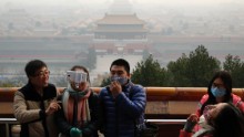 Visitors, some wearing masks to protect themselves from pollutants, share a light moment as they take a selfie at the Jingshan Park on a polluted day in Beijing on December 7, 2015, the day Beijing's city government issued its first red alert for pollution, the highest level of warning.