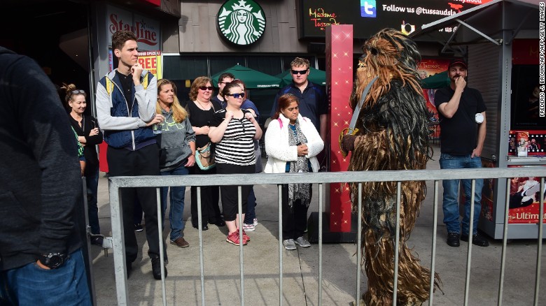 Bystanders watch as a person dressed in a Chewbacca costume walks near where fans have been congregating at the plaza in front of the TCL Theatre.