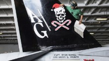 Aviation Structural Mechanic Airman V. Sek, assigned to the "Jolly Rogers" of Strike Fighter Squadron (VFA) 103, applies a Christmas decal to an F/A-18F Super Hornet in the hangar bay of the Nimitz-class aircraft carrier USS Harry S. Truman in December 2015.