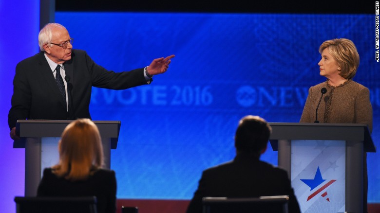 Sanders speaks as Clinton looks on during the debate. Sanders, at the start of the debate, apologized to Clinton for his staff&#39;s exploitation of a Democratic National Committee computer vendor&#39;s glitch to access her campaign&#39;s proprietary voter files.