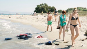 Tourists stroll the beach walk past abandoned lifejackets of refugees, August 2015 Kos, Kos Island, Greece, Europe