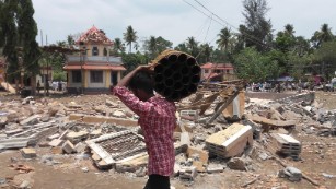 A man carries empty fireworks shells past a collapsed building after Sunday&#39;s temple fire