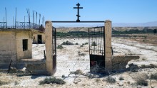 The rusted gate of the Russian Orthodox church looks out onto the Jordan River and the Jordanian mountains beyond. After the fields are cleared, each church will have its own walking path to the river.