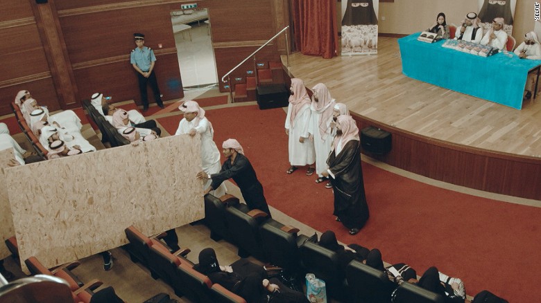 Scene shows men and women being separated by a makeshift wall