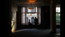 Two people take in the convention scene from a window in a bar.