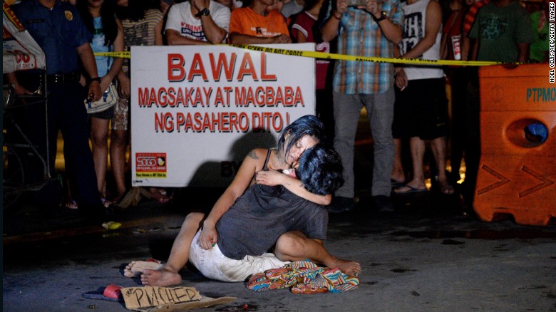 A woman cradles her husband, next to a placard which reads &quot;I&#39;m a pusher,&quot; who was shot dead in Manila on July 23, 2016. 