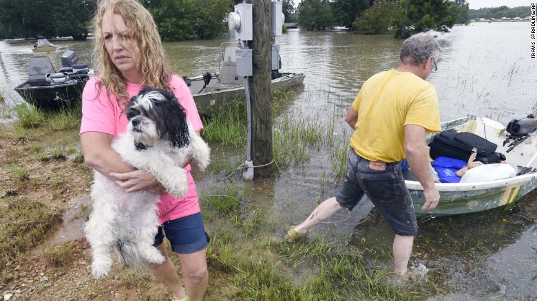 Tammie Wise holds her dog Mikey, after Jeffrey Lesage, right, boated them to safety in Central, La., Saturday, Aug. 13, 2016. Louisiana Gov. John Bel Edwards says more than 1,000 people in south Louisiana have been rescued from homes, vehicles and even clinging to trees as a slow-moving storm hammers the state with flooding. (Travis Spradling/The Advocate via AP)