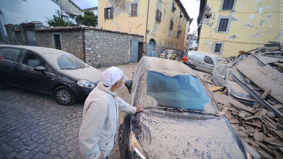 A man surveys damage near a dust-covered car in Amatrice on August 24.