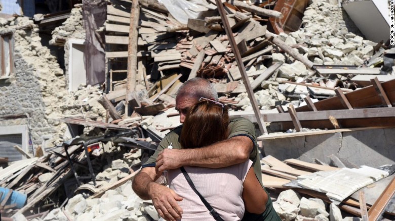 Two people hug each other next to damaged houses in Pescara del Tronto.