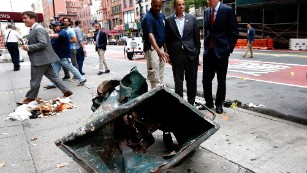 New York Mayor Bill de Blasio, right, and New York Gov. Andrew Cuomo, second right, look over the mangled remains of a dumpster Sunday, September 18, in New York&#39;s Chelsea neighborhood. An explosion injured 29 people there the night before.