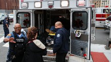 Emergency workers help an injured person into an ambulance outside the station.