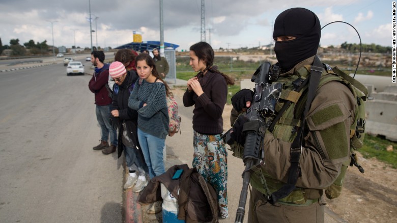 An Israeli soldier stands guard as Israeli settlers stand at a bus station in the West Bank.