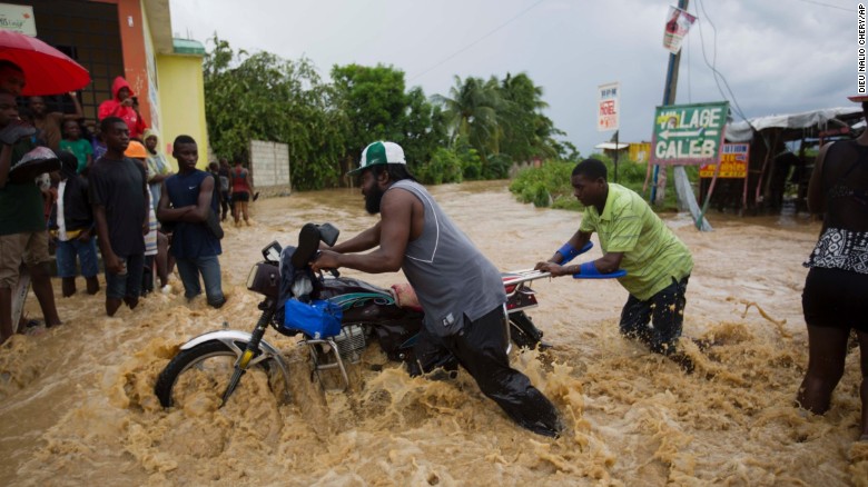 Men push a motorbike through a flooded street in Leogane on Wednesday, October 5.