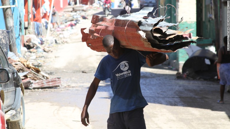 A man carries perforated roof pieces on his shoulders to clear the wreckage after Hurricane Matthew.