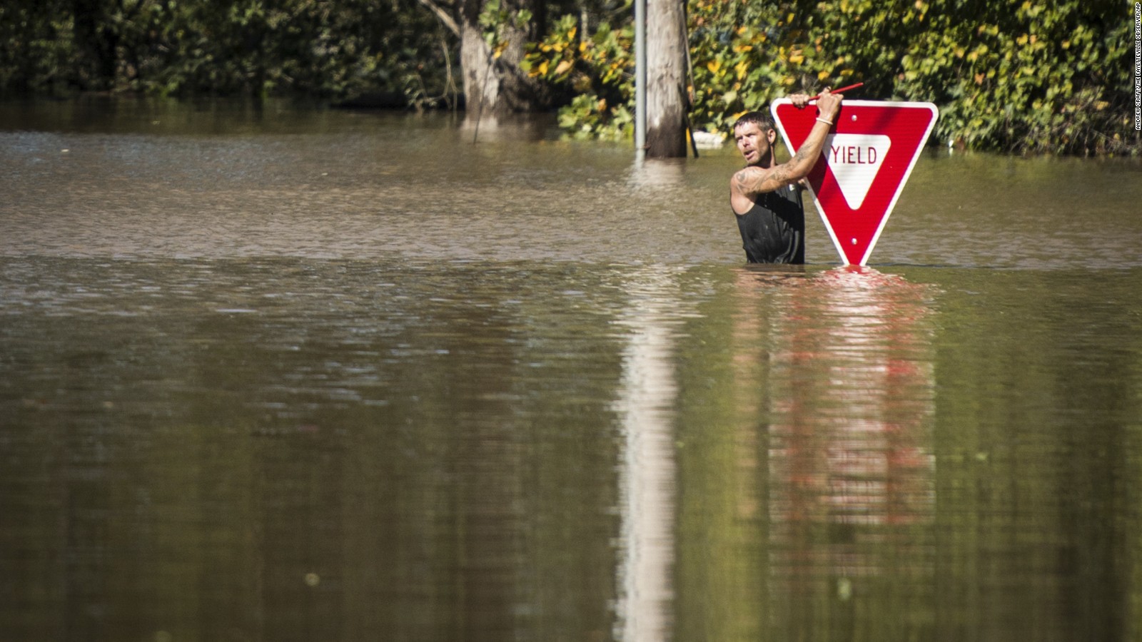 A man holds onto a sign after trying to swim out to help a stranded truck driver in Hope Mills, North Carolina, on Sunday.