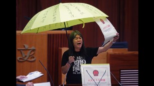Leung Kwok-hung, holds a yellow umbrella and an oversized mock copy of the proposed anti-subversion legislation as she takes oath.