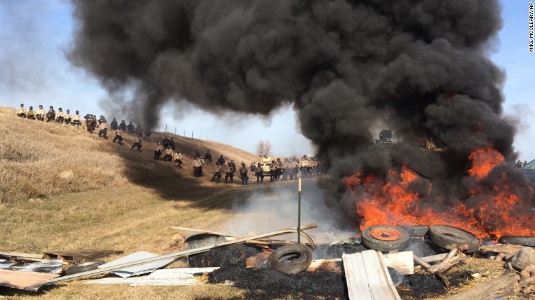 Tires burn as armed soldiers and law enforcement officers stand in formation on Thursday, Oct. 27, 2016, to force Dakota Access pipeline protesters off private land where they had camped to block construction. The pipeline is to carry oil from western North Dakota through South Dakota and Iowa to an existing pipeline in Patoka, Ill. (Mike McCleary/The Bismarck Tribune via AP)