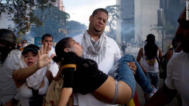 A man carries a woman overcome by tear gas from riot police at anti-government protesters in Caracas on Saturday, February 22. 