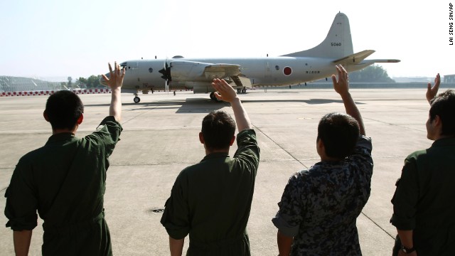 Ground crew members wave to a Japanese Maritime Defense Force P3C patrol plane as it leaves the Royal Malaysian Air Force base in Subang, Malaysia, on Sunday, March 23, heading for Australia to join a search and rescue operation for missing Malaysia Airlines Flight 370. The search is entering its third week with no indication of the fate of the aircraft.