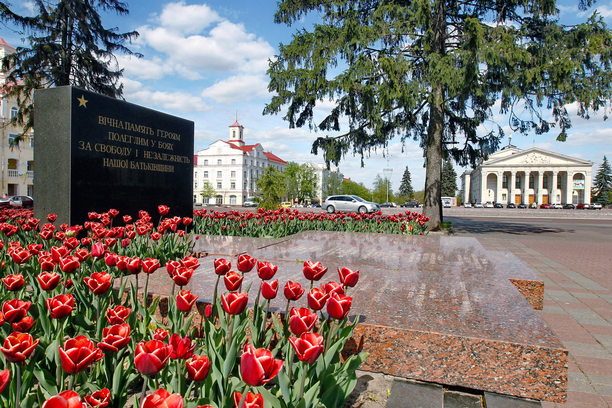 Bright red tulips around a black stone memorial, official building in the background
