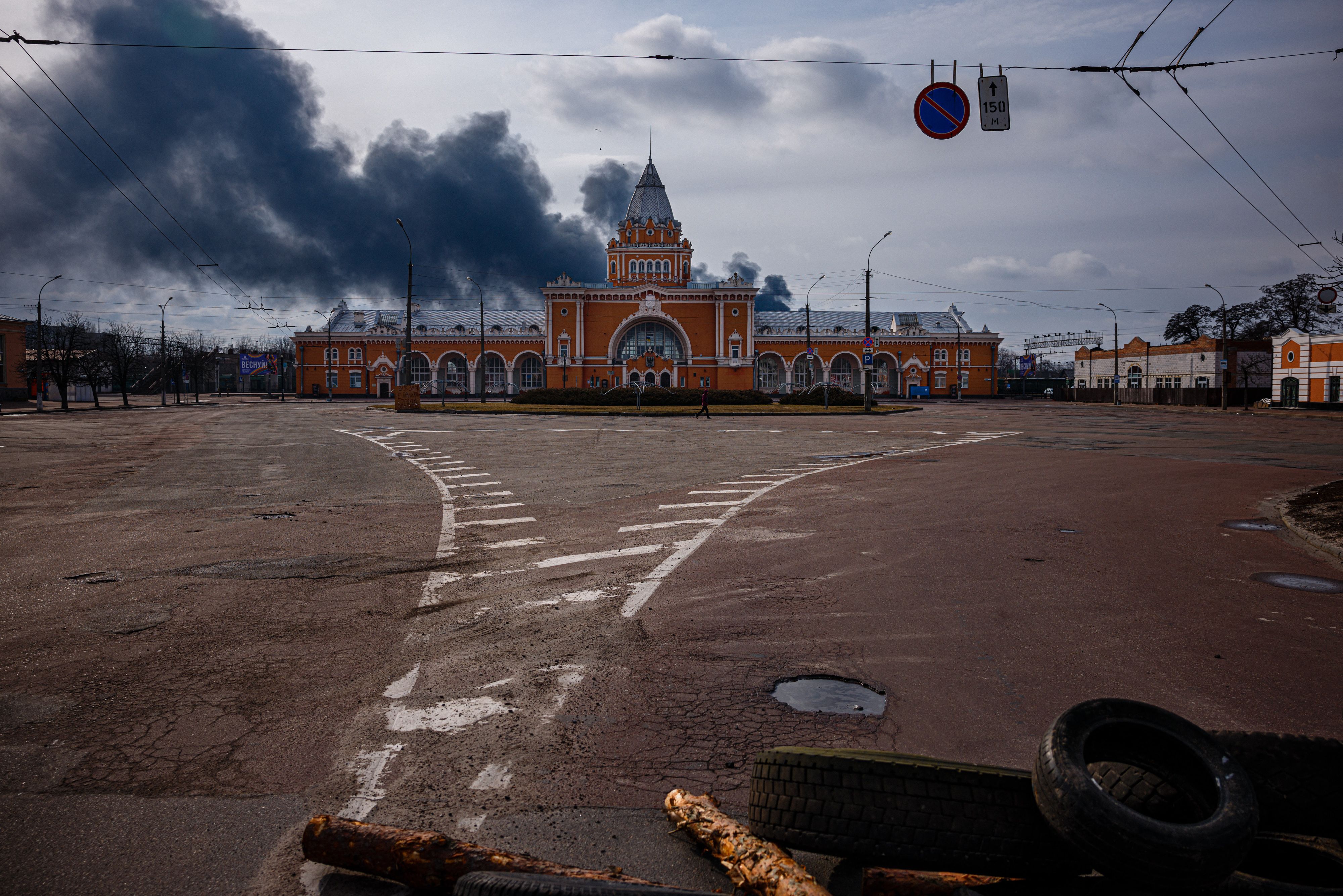 A large red building with arches has black smoke behind it