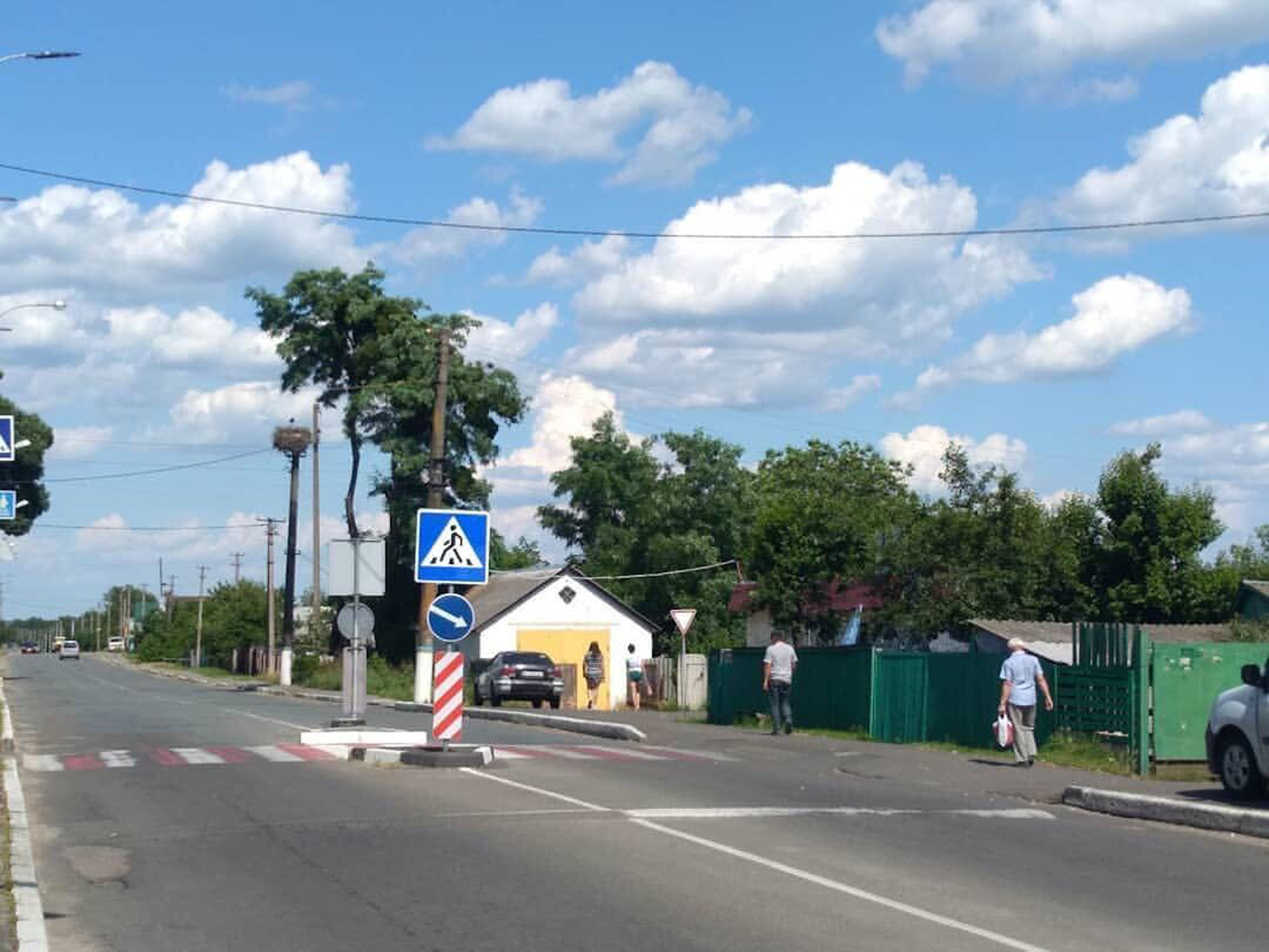 A two-lane road with three people casually walking on the pavement