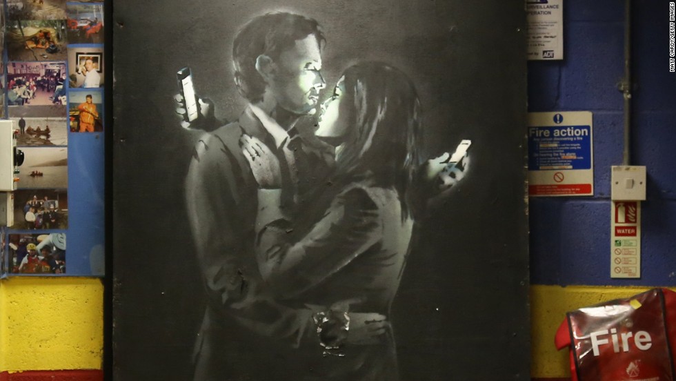 A Banksy work appears at a youth center in Bristol, England, in April 2014. Called &quot;&lt;a href=&quot;http://www.cnn.com/2014/04/16/world/europe/uk-art-banksy-removed/index.html&quot;&gt;Mobile Lovers&lt;/a&gt;,&quot; it features a couple embracing while checking their cell phones. Members of the youth center took down the piece from a wall on a Bristol street and replaced it with a note saying the work was being held at the club &quot;to prevent vandalism or damage being done.&quot; The discovery came shortly after another image believed to be by Banksy surfaced in Cheltenham, England.