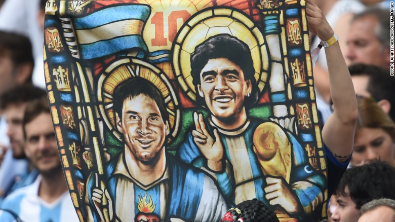 Lionel Messi and Diego Maradona depicted as saints on a supporter&#39;s flag. Maradona holds the World Cup trophy while Messi, crucially, does not. 