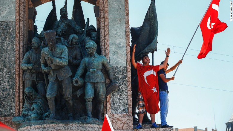 People protesting against the coup wave a Turkish flag on top of the monument in Taksim Square.