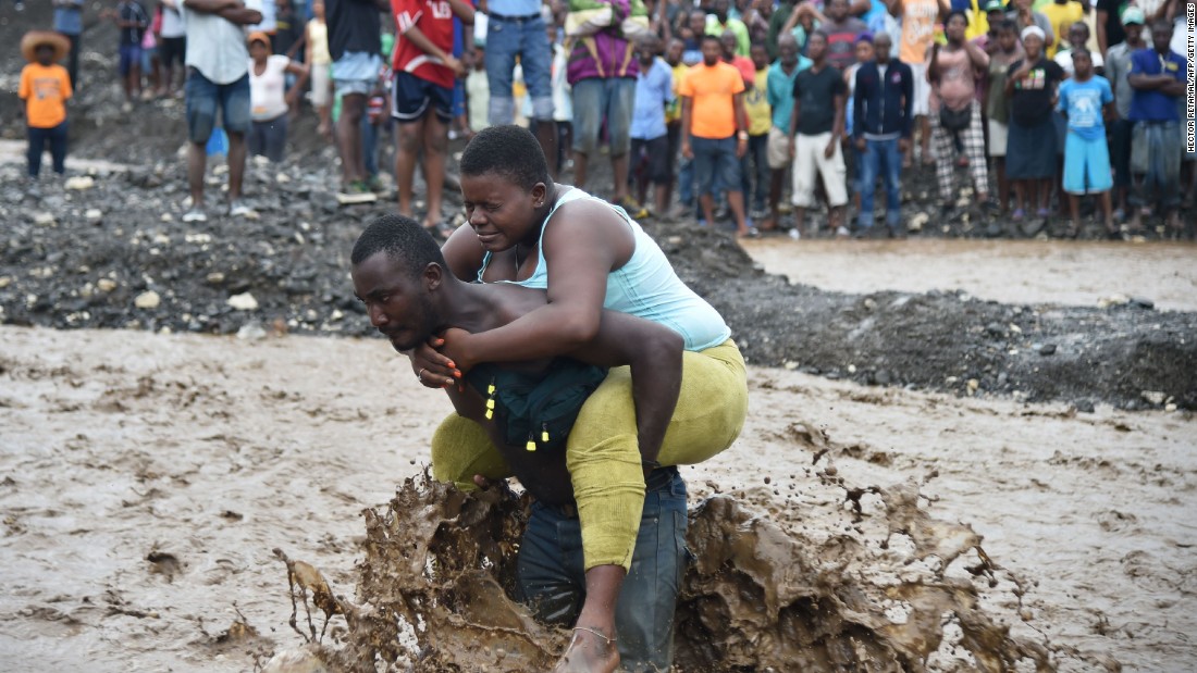 A man carries a woman across a river at Petit Goave where a bridge collapsed during the rains of the Hurricane Matthew. CNN