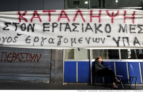 An employee sits by the occupied Ministry of Finance in Athens by a banner which translates as 'Occupation' on September 30, 2011